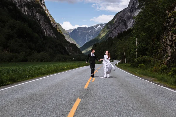 Nowożeńcy Trzymający Się Ręce Biegną Wzdłuż Środka Autostrady — Zdjęcie stockowe
