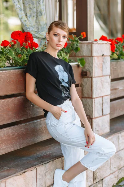 A model in a black t-shirt stands on a summer street