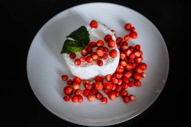 Beyaz bir tabakta bir sürü kırmızı çilek ve dondurma var. Üstünde nane yaprağı olan.