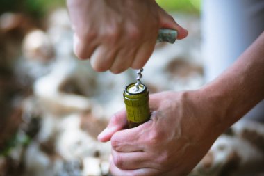 Metal bir tirbuşonla şarap şişesini açan bir adamın elleri.