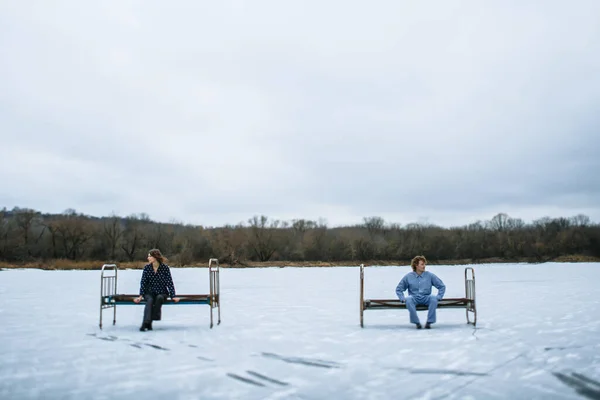 A guy and a girl in pajamas are on the ice of a frozen lake. People sit on an iron bed on the ice.