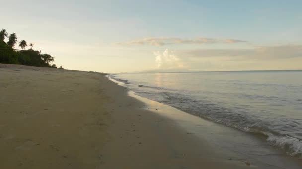 Onde di mare che rotolano sotto il sole alla spiaggia sabbiosa. Spiaggia tropicale con tramonto e cielo azzurro. — Video Stock