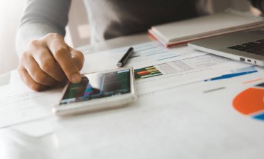 İş kadını, şirket ofisindeki akıllı telefon ve bilgisayar laptopunu kullanarak iş raporu grafiklerini ve finans şemasını analiz eder..