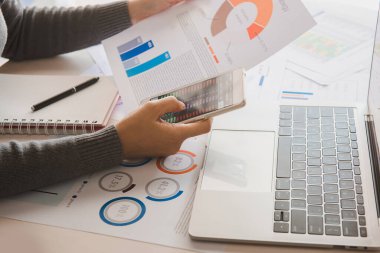 İş kadını akıllı telefonu elinde tutuyor ve elindeki belgeleri inceliyor. Finansal ve yatırım kavramı.