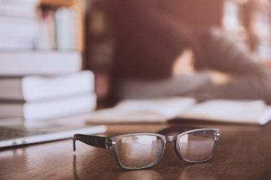 Gözlükler bulanık, arka planda bir yığın kitap ve dizüstü bilgisayarın yanında uyuyan genç bir kız..