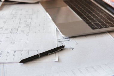 Projelerin taslakları, dizüstü bilgisayarı ve bir kalemle planların yakın plan görüntüsü.