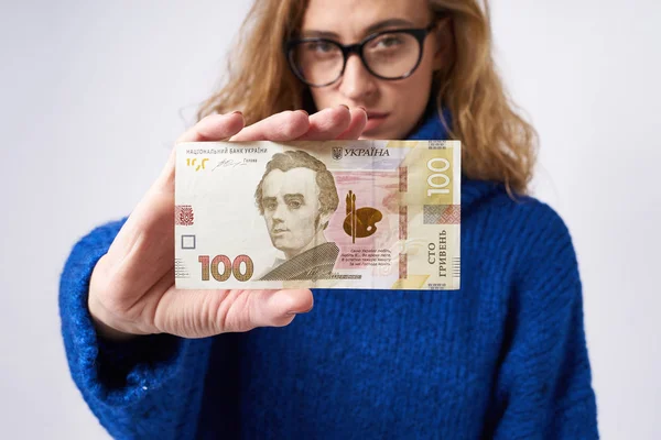 Gözlüklü sarışın kız kameraya bakar ve Ukraynaca 100 hryvnia elinde tutan