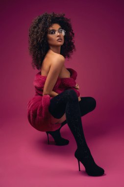 Parlak bir arka planda oturan bir kürk ve botlar yarım çıplak model