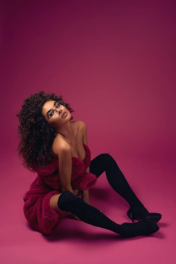 Parlak bir arka planda oturan bir kürk ve botlar yarım çıplak model