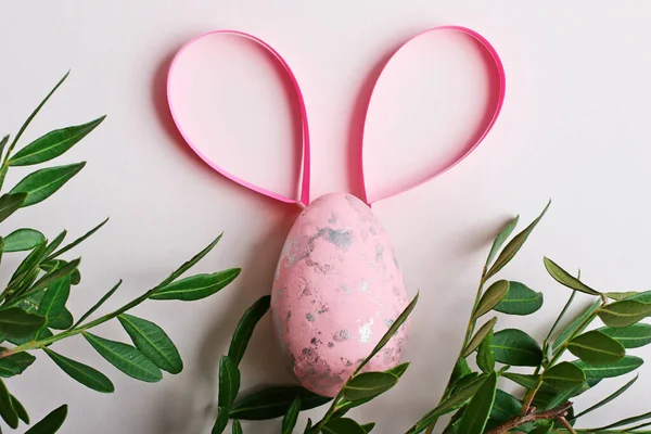 Uovo di Pasqua rosa con orecchie di carta come un coniglio.Fogliame fresco sullo sfondo.. — Foto Stock