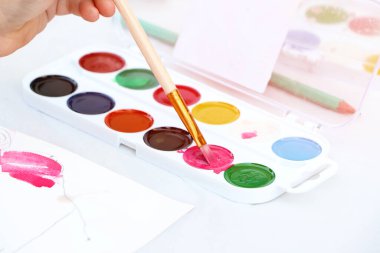 Bir çocuk boya fırçasıyla birlikte boya ve çizim aletleri tutuyor. Bir çocuğun elinin fotoğrafını çek. Okula geri dön..