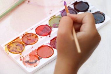 Bir çocuk boya fırçasıyla birlikte boya ve çizim aletleri tutuyor. Bir çocuğun elinin fotoğrafını çek. Okula geri dön..