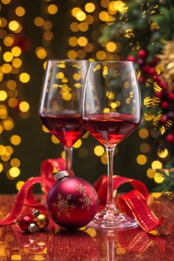 Şarap kadehlerinde kırmızı şarap ve tatil ışıklarına karşı Noel topu..