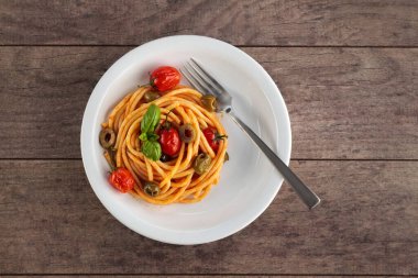 Domates soslu spagetti ve koyu ahşap bir yüzey üzerinde beyaz bir kasede fesleğen.