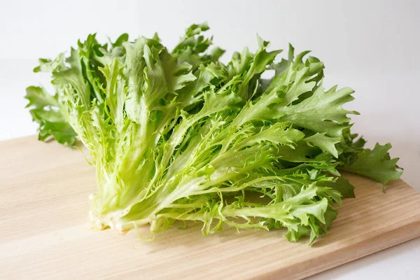 Un mazzo di lattuga fresca sul tagliere di legno sullo sfondo bianco. Insaporire i verdi sul tavolo. Cibo vegetariano sano. Un ingrediente per insalata . — Foto Stock