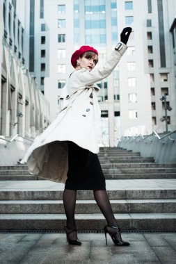 Şehrin iş merkezinin yanındaki merdivenlerde yürüyen açık renk pelerinli, siyah elbiseli, kırmızı bereli genç zarif bir kızın arkası. Bahar günü. Yüksek topuklu iş kadını arkasına bakıyor. Yaşam biçimi. 