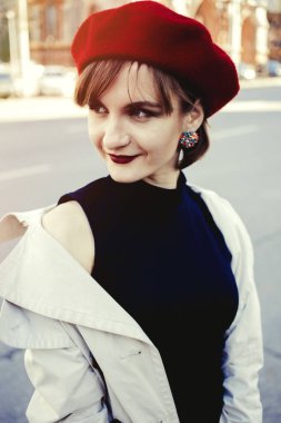 Kırmızı dudaklı, kırmızı bereli ve sokakta pelerinli, siyah elbiseli, gülümseyen genç bir bayan. Mutluluk. Kızım. Şehirde bahar güneşli bir gün.. 