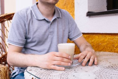Kafenin üzerinde beyaz peçete örgü örülmüş bir şekilde adamın elleri üzerinde kahve. Mesaj için yer. Kafede oturan bir adam. Kafasız.