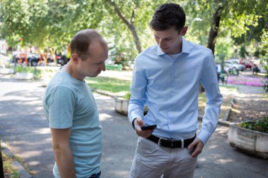 İki adam sokakta güzelce konuşur ve telefona bakar. Bir Amerikalı ve bir Avrupalı. İki meslektaşım şehirde tanıştı. Tanıdık.. 