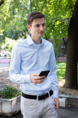 Şehirde mavi gömlekli gülümseyen bir adamın portresi. Elinde telefon ve arka planda ağaçlar vardı. Konuşmadaki adam, dikkatle dinliyor. Amerika ya da Avrupa 'da yaz günü