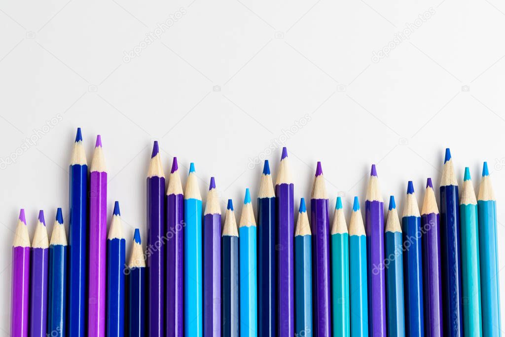 Mixed light and dark blue, purple, cyan and teal colored pencils arranged in line, isolated on white, children school or office suppliers photographed with soft focus from side view, with copy space
