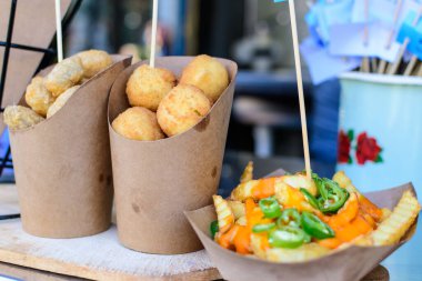 Kahverengi kağıt koni içinde Sicilya arancini grubu ve peynir kremalı patates kızartması ve jalapenos biberleri doğrudan güneş ışığı altında bir sokak yemeği pazarında, seçici bir odak noktası.