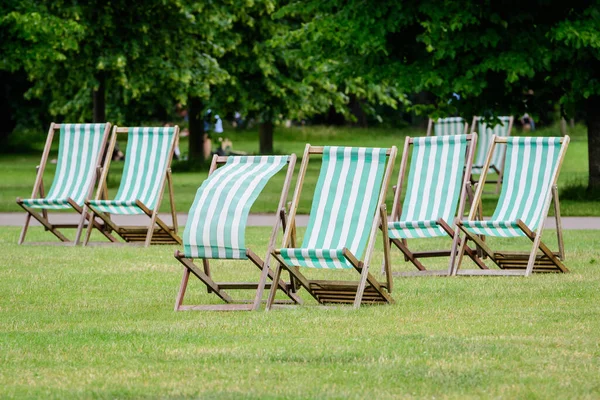 Six white and green striped outdoor garden chairs displayed in fresh green grass in a park in London, Great Britain, during a sunny summer day, natural green background in a big city