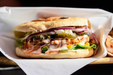 Lezzetli bir hamburger veya burger sandviçi, ızgara baharatlı et, mayonez, salatalık turşusu, kırmızı soğan ve yeşil salata, bir sokak yiyecek pazarında satılıyor, seçici bir odak noktası var.