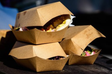 Üç paket kahverengi karton kutu bir sokak yiyecek pazarındaki ahşap bir masada sergileniyor, satılmaya hazır ve sağlıklı yiyecekler yiyor.