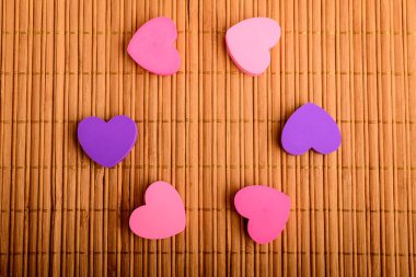 Kahverengi bambu masa dekorasyonunda altı pembe ve leylak rengi kalp yuvarlak bir dairede sergileniyor, sağ tarafta yazı için yer var, seçici odaklanma.