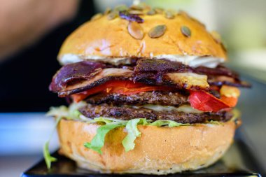 Lezzetli bir hamburger sandviçi, domatesli, salatalı ve pastırmalı ızgara et, hafta sonu sokak yemekleri pazarında satılıyor, seçici bir odak noktası.