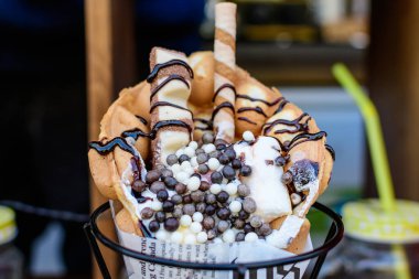 Şekerleme, çikolata şurubu, gofret ve krema içeren bir waffle 'ı bir sokak yiyecek pazarında sergileyin.