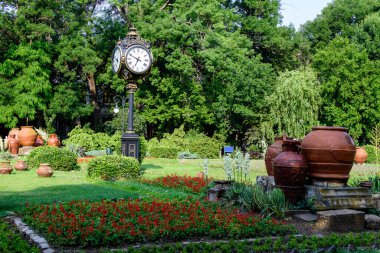 Romanya 'nın Bükreş kentindeki Cismigiu Garden' da güneşli bir yaz gününde canlı kırmızı çiçekler, yeşil ağaçlar ve çimlerle ana giriş