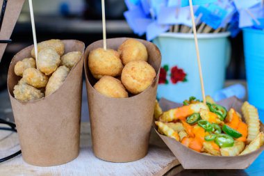 Kahverengi kağıt külahta Sicilya arancini grubu ve peynir kremalı patates kızartması ve doğranmış jalapanelos. Doğrudan güneş ışığı altında bir sokak yemeği pazarında, seçici bir odak noktası.