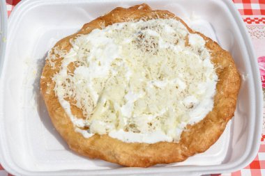 Bir langoya yakın, tipik Macar yemek spesiyali, masada beyaz bir tabakta ekşi krema ve peynir, yiyecek pazarında güneşte kızartılmış hamur. 