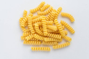 Kurutulmuş fusili İtalyan makarnası, beyaz bir masada gelişigüzel sergileniyor, pişirilmeye hazır, masa arkasında izole edilmiş, üst manzaralı.