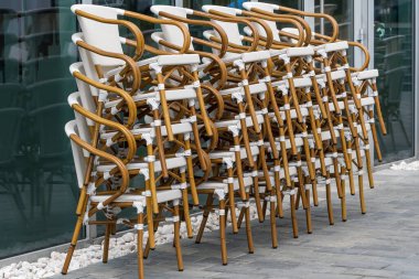 Açık hava manzaralı bir kahve dükkanının yanında dikey olarak sergilenen büyük bir grup temiz ahşap sandalye.