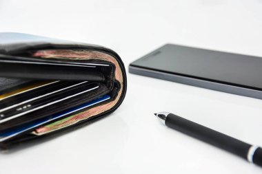 kahverengi erkek deri cüzdanı kart, banknot, beyaz arka planda kalem ve cep telefonu, teknoloji online bankacılık para transferi, e-ticaret konsepti, kopyalama alanı (seçici odak noktası))