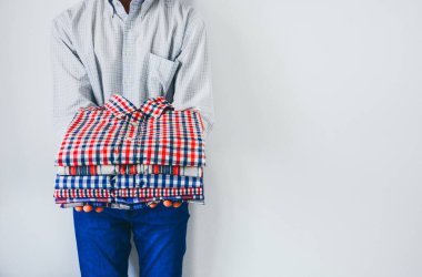 Ellerinde katlanmış renkli ekose gömlek yığını, ellerinde katlanmış giysiler tutan adam beyaz arka planda, kopyalama alanı