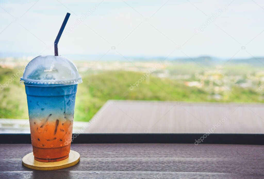 glass of colorful iced Thai milk tea mixed with butterfly pea juice on wooden table with natural blur background, copy space