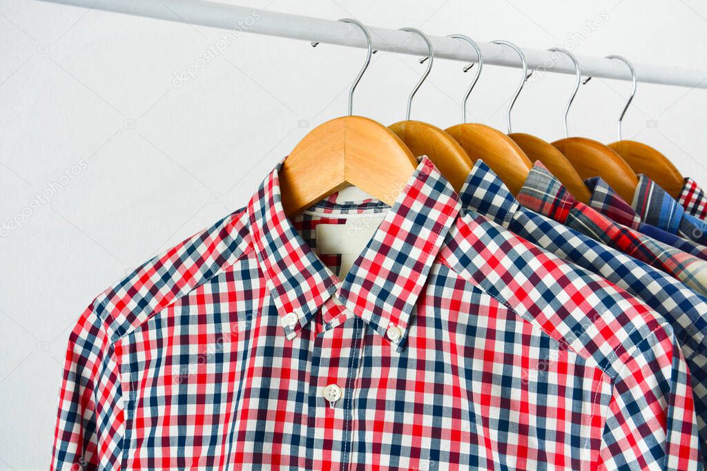 close up clothes hang on shelf or clothing rack, long sleeve red and blue checkered shirt on wooden hanger over white background, copy space