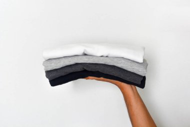 Katlanmış siyah, gri ve beyaz renk tonunu (monokrom) beyaz arkaplan üzerindeki eldeki tişört yığınını kapat, boşluğu kopyala