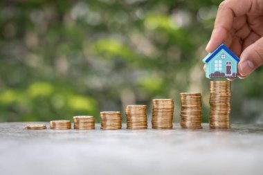 Para Finansal, İş Büyümesi, Kredi ve Gayrimenkul Yatırım Konsepti. Adam ev modelini bozuk para yığınına altın paraların üzerine koydu.