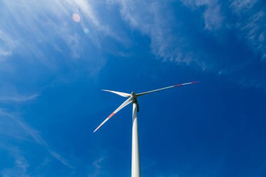 Mavi gökyüzünün önünde bir rüzgar türbini dönüyor.