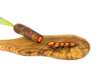 Beyaz bir arka plana karşı zeytin tahtasında siyah bir havuç.