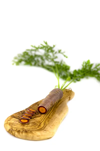 Beyaz bir arka plana karşı zeytin tahtasında siyah bir havuç.