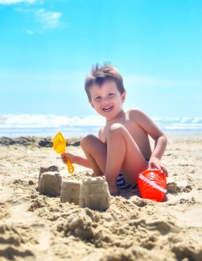 Bir çocuk kumla oynar ve deniz kıyısında kumdan kaleler inşa eder. Yaz havası