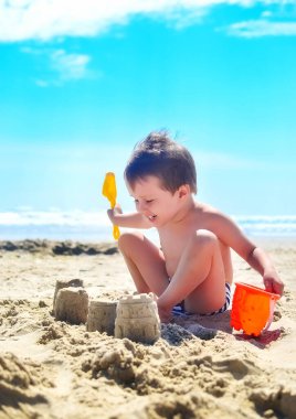 Bir çocuk kumla oynar ve deniz kıyısında kumdan kaleler inşa eder. Yaz havası