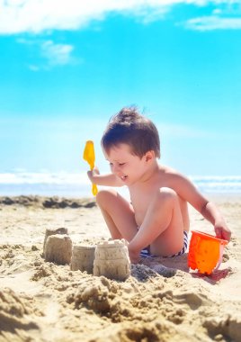 Bir çocuk kumla oynar ve deniz kıyısında kumdan kaleler inşa eder. Yaz havası