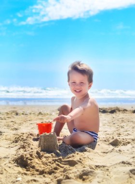 Bir çocuk kumla oynar ve deniz kıyısında kumdan kaleler inşa eder. Yaz havası